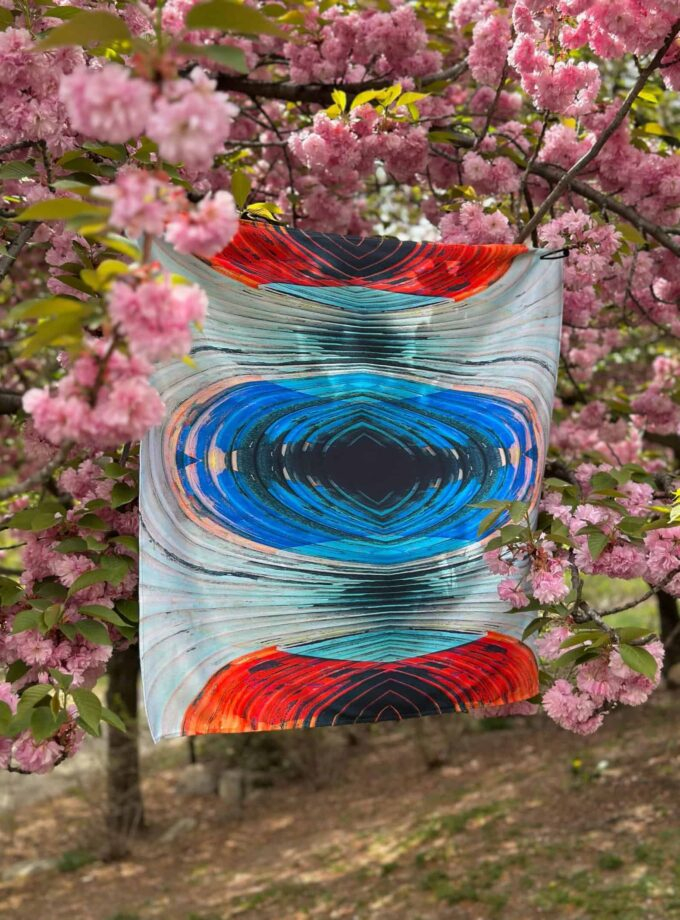 Vibrant abstract glass art piece hanging among pink cherry blossom branches, showcasing colorful swirling designs and intricate craftsmanship.