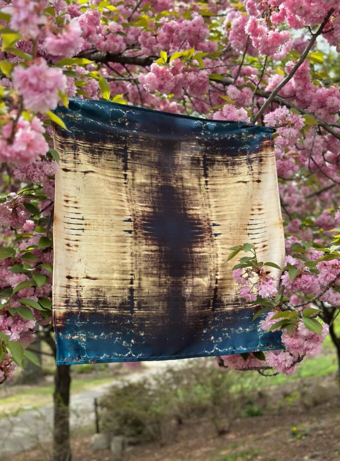Pink cherry blossom tree with a custom tie-dye scarf hanging among the branches, showcasing a vibrant outdoor display of floral beauty and artisanal textile art.