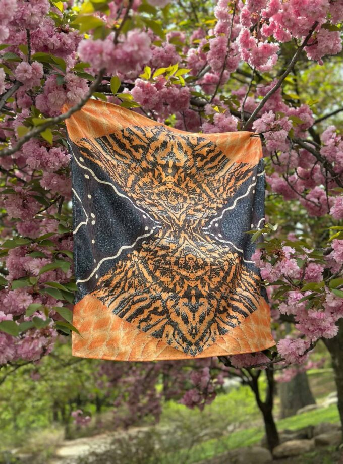 Vibrant butterfly-themed scarf hanging on a tree branch with pink blossoms, showcasing colorful, artistic design perfect for fashion and nature lovers.
