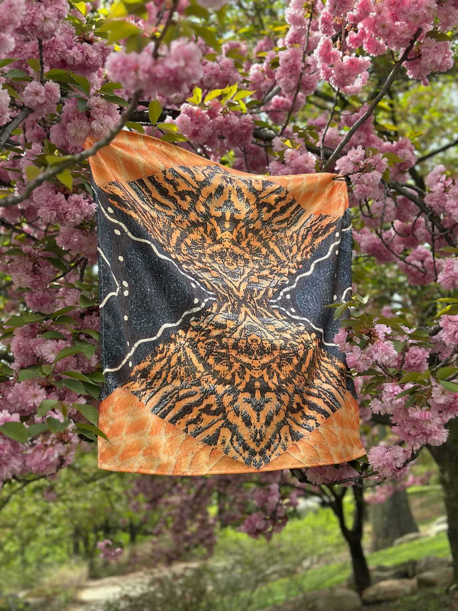 Vibrant butterfly-themed scarf hanging on a tree branch with pink blossoms, showcasing colorful, artistic design perfect for fashion and nature lovers.