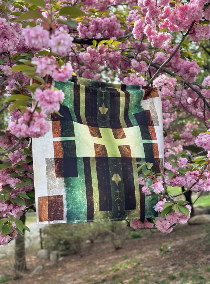 Colorful abstract fabric art hanging among vibrant pink cherry blossom tree flowers, showcasing unique textile design and outdoor nature, perfect for springtime decor and artistic expression.