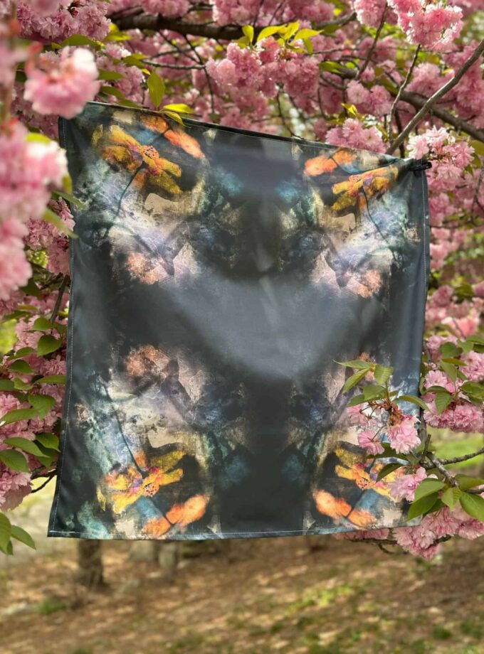 Vibrant colorful scarf with abstract design hanging on a blooming pink cherry blossom tree. Perfect for adding artistic flair to your wardrobe or home decoration.