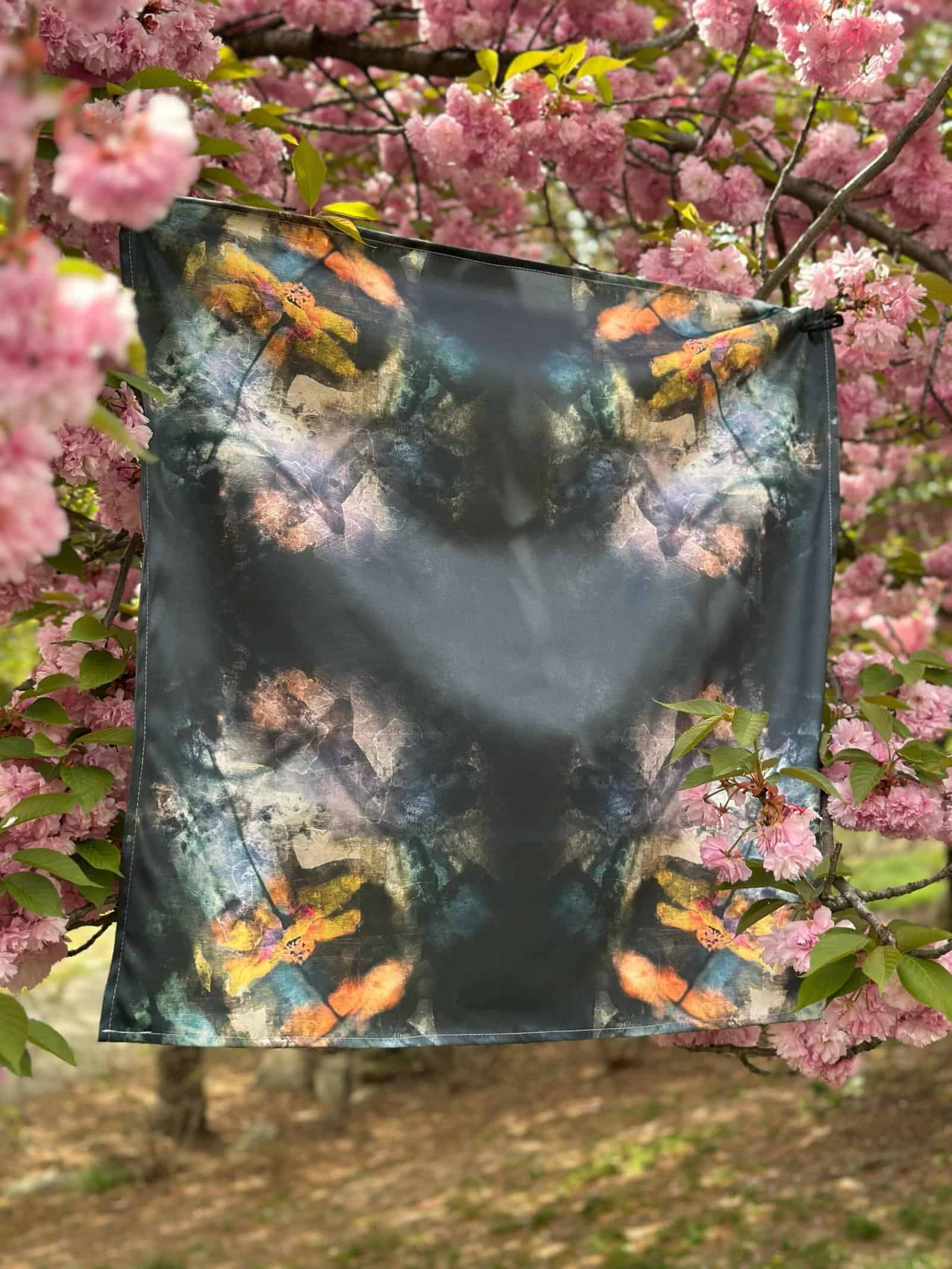 Vibrant colorful scarf with abstract design hanging on a blooming pink cherry blossom tree. Perfect for adding artistic flair to your wardrobe or home decoration.