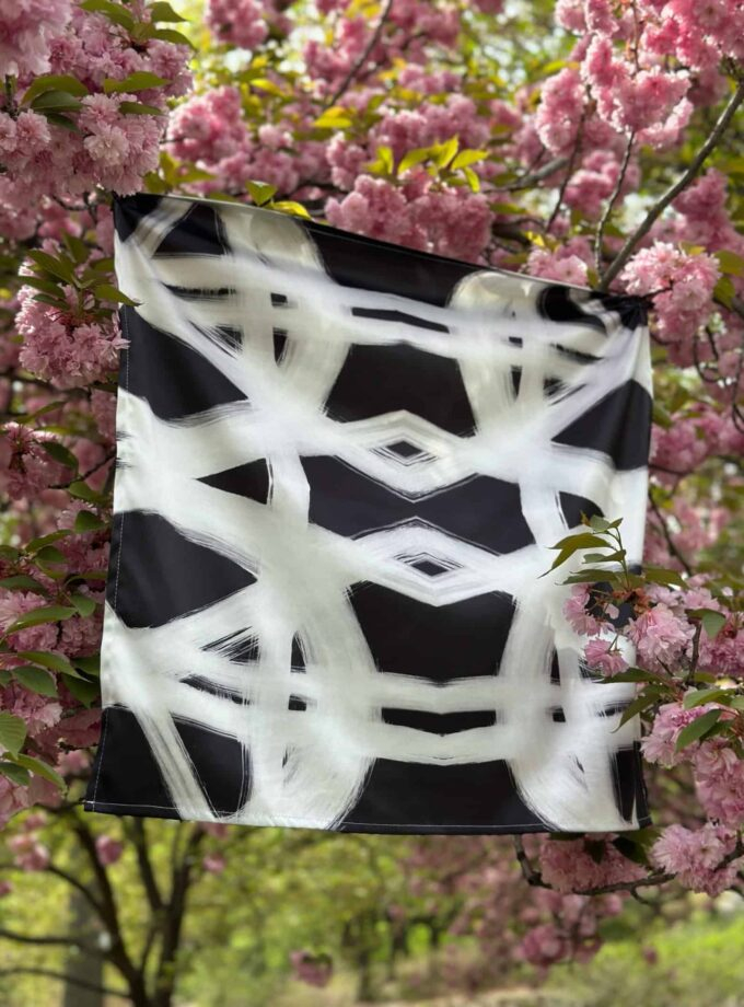 Vibrant black and white abstract patterned scarf hanging among pink cherry blossoms. Elegant accessory with artistic design, perfect for spring fashion and outdoor style.
