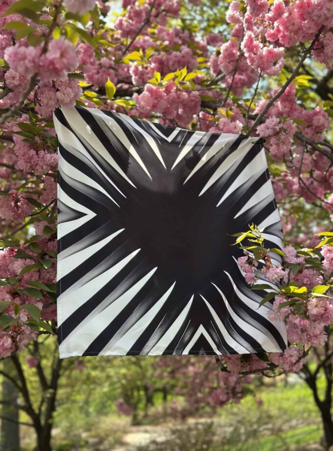 Vibrant black and white geometric patterned flag hanging among blooming pink cherry blossoms in spring, creating a striking contrast and a lively outdoor scene.