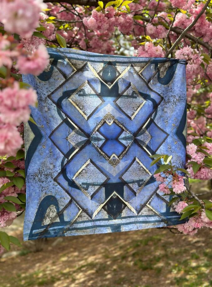 Vivid blue geometric patterned scarf hanging among blooming pink cherry blossoms, showcasing vibrant colors, intricate design, and artistic style perfect for spring fashion and outdoor photography.