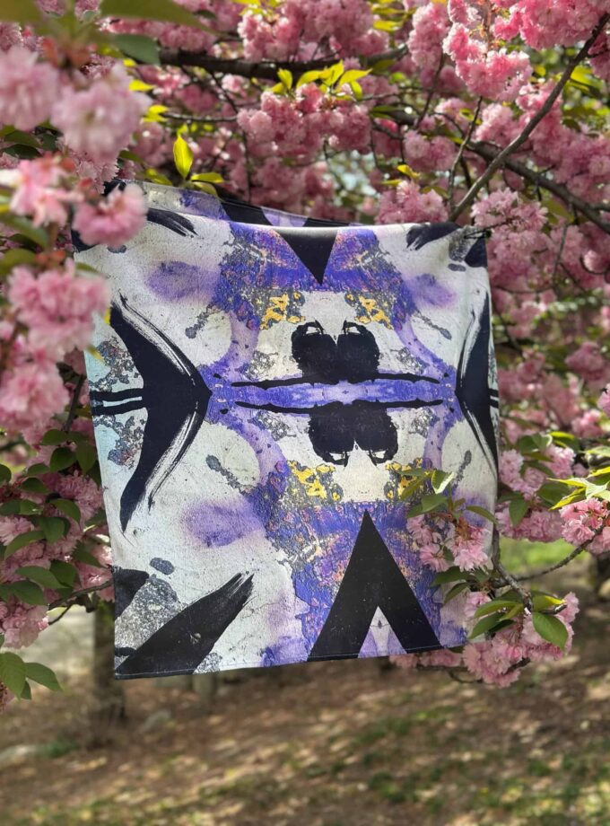 Vivid artistic fabric artwork hanging on a tree branch surrounded by vibrant pink cherry blossoms, showcasing creative textile art and nature-inspired design with bold colors and abstract patterns.