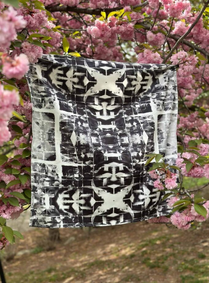 Vibrant black and white tie-dye scarf hanging on a cherry blossom tree branch, showcasing boho-chic fashion accessories with floral backdrop.