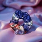 Vibrant abstract scrunchie with a mix of blue, red, white, and yellow colors, set against soft pink satin fabric, showcasing artistic and colorful hair accessories from Confiture.