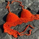 Orange crochet bikini top on rocky surface, summer beachwear, handmade swimsuit, vibrant swimwear, crochet clothing accessory, Confiture NYC.