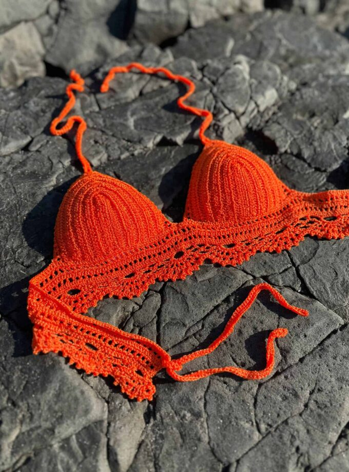 Orange crochet bikini top on rocky surface, summer beachwear, handmade swimsuit, vibrant swimwear, crochet clothing accessory, Confiture NYC.