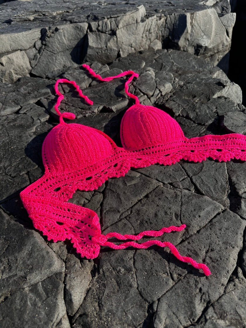 Bright pink handmade crochet bikini top on rocky surface, ideal for summer beachwear, swim accessories, and stylish poolside fashion. Perfect for beach vacations and outdoor leisure.