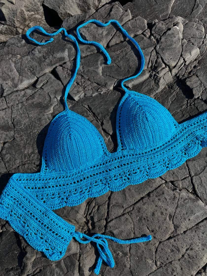 Handmade blue crochet bikini top on dark rocky surface, emphasizes artisanal swimwear, vibrant color, and unique design. Perfect for summer beach fashion and boho style enthusiasts.
