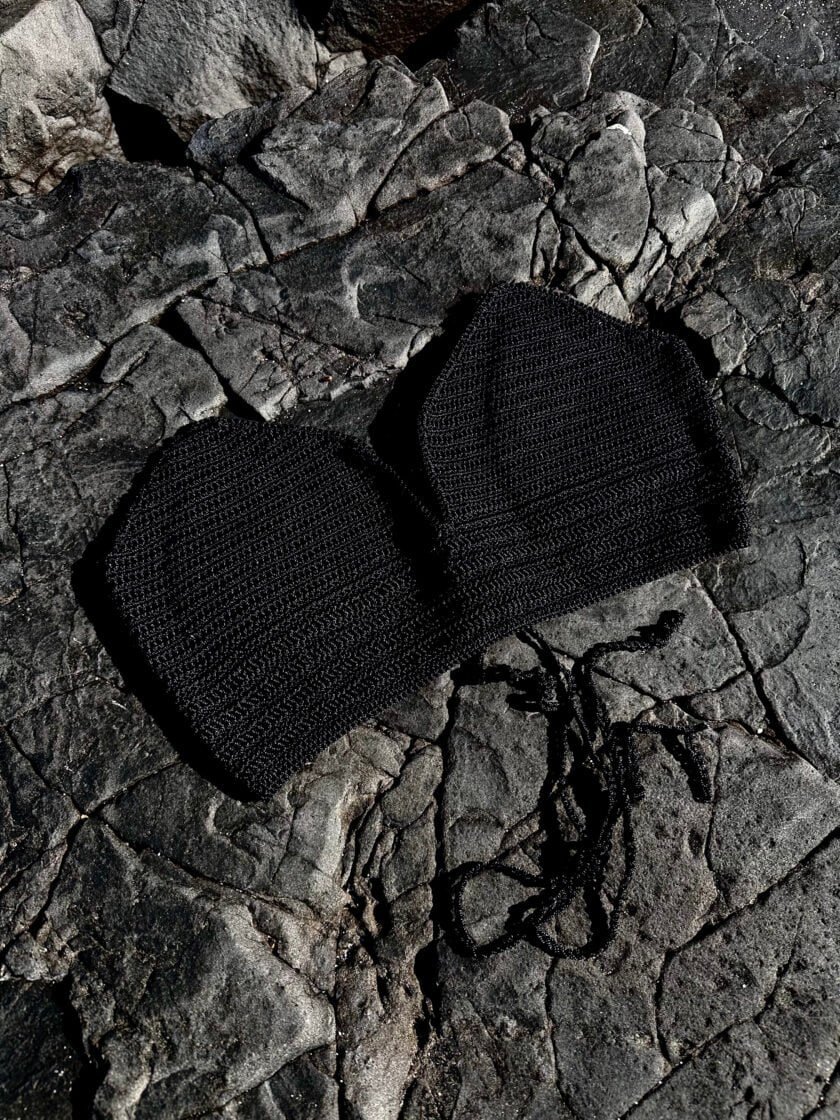 Vegan black knit face mask lying on dark rocky surface, stylish and eco-friendly protective accessory for health and fashion.