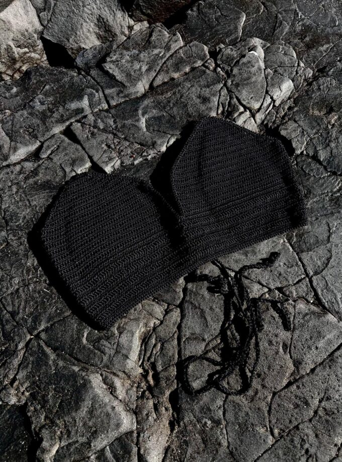 Vegan black knit face mask lying on dark rocky surface, stylish and eco-friendly protective accessory for health and fashion.