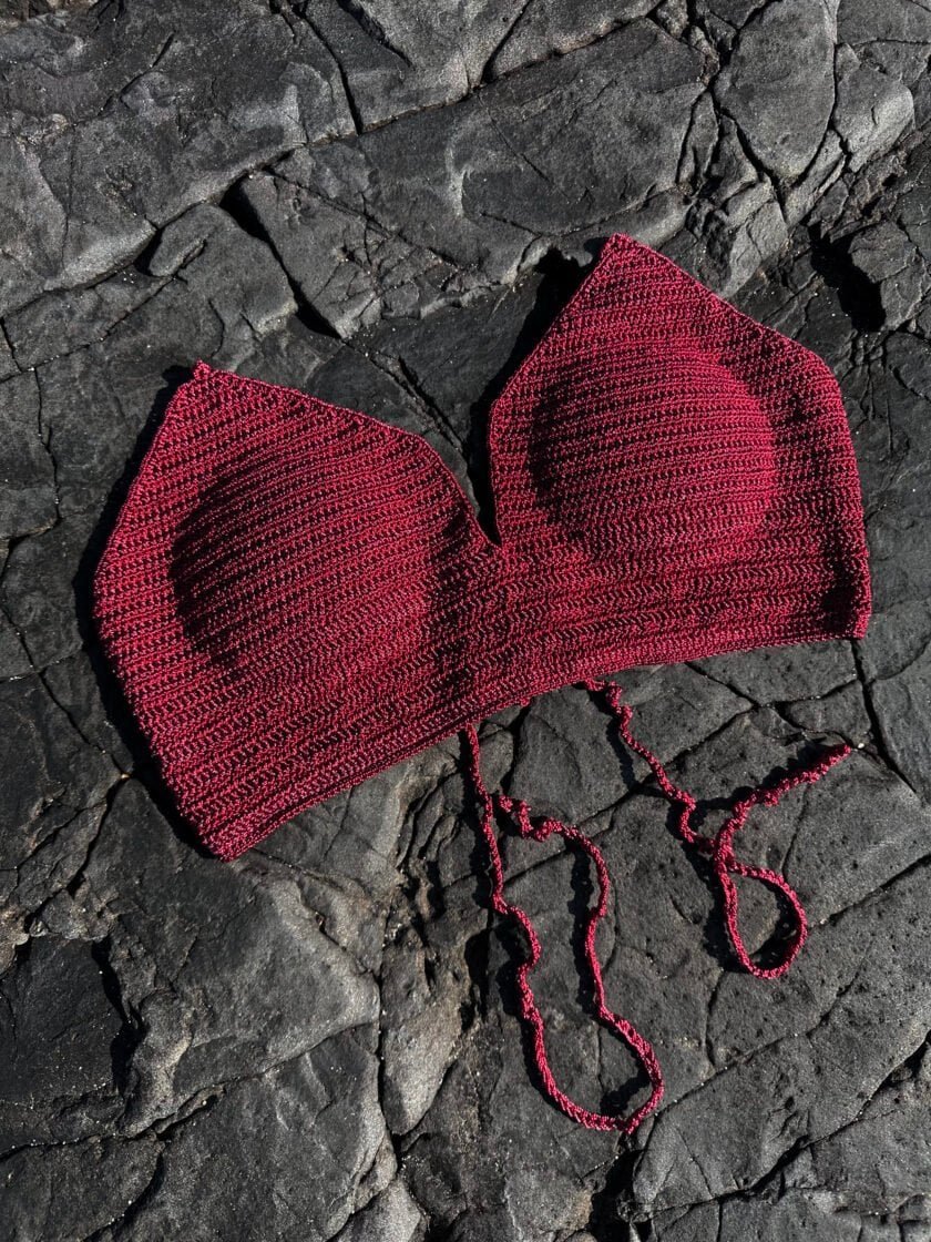 Soft knit red bikini top with adjustable ties, laid on black textured rocks, perfect for summer beachwear and swimwear fashion.
