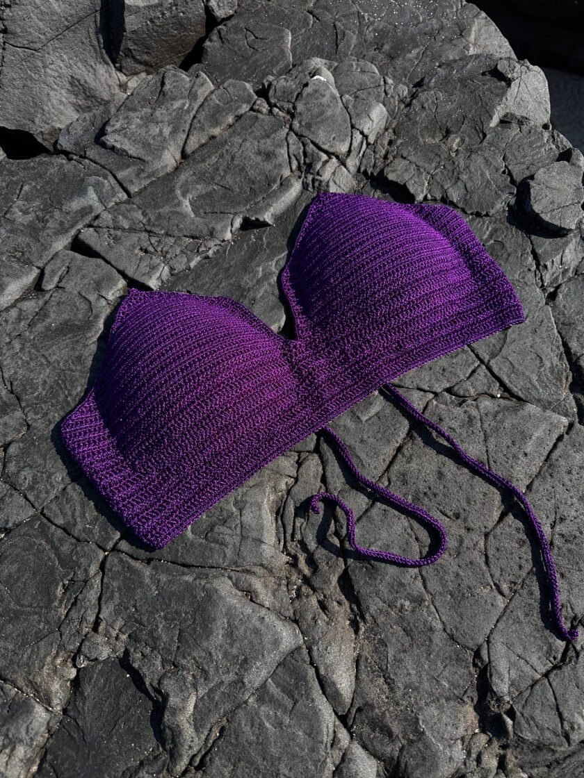 Violet knit face mask draped over dark textured rocks, showcasing stylish accessory for fashion and protection.