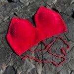 Red knitted heart-shaped hat on dark rocky surface, soft and cozy accessory, perfect for Valentine's Day or romantic gift, made with high-quality yarn, stylish and unique design.
