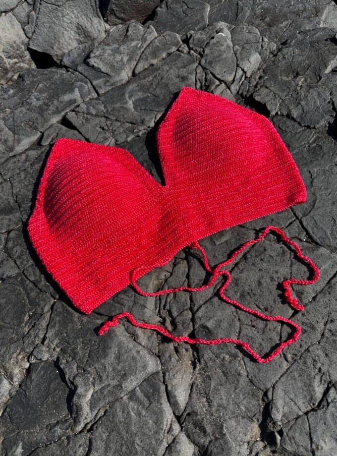Red knitted heart-shaped hat on dark rocky surface, soft and cozy accessory, perfect for Valentine's Day or romantic gift, made with high-quality yarn, stylish and unique design.