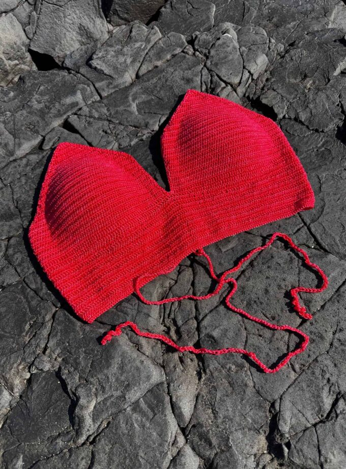 Red knitted heart-shaped hat on dark rocky surface, soft and cozy accessory, perfect for Valentine's Day or romantic gift, made with high-quality yarn, stylish and unique design.