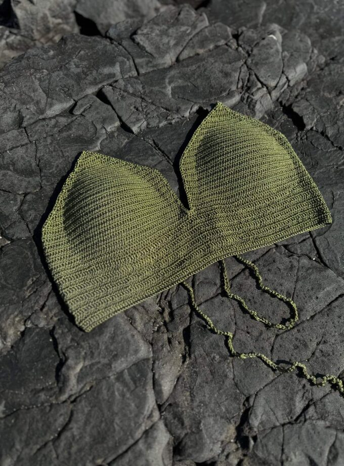 A stylish green beaded handbag resting on dark, cracked volcanic rocks, showcasing a modern accessory perfect for casual or evening wear with intricate beadwork details.