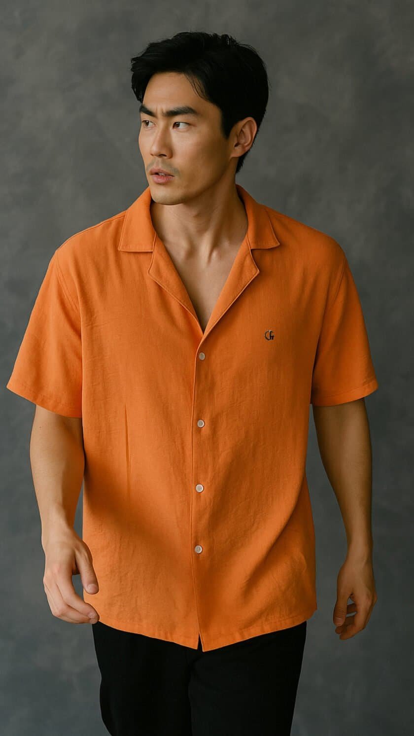 Orange shirt with a small embroidered logo on the chest, modern men's fashion, stylish casual wear, lightweight linen fabric, short-sleeve button-up, summer clothing, fashion photography, grey textured background.