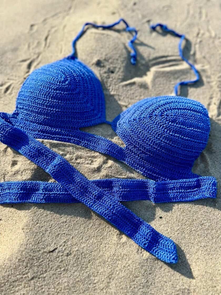 Bright blue woven bikini top on sandy beach, summer swimwear accessory, stylish beachwear, vibrant swimwear for women, perfect for beach vacation, Confiture NYC inspired fashion.