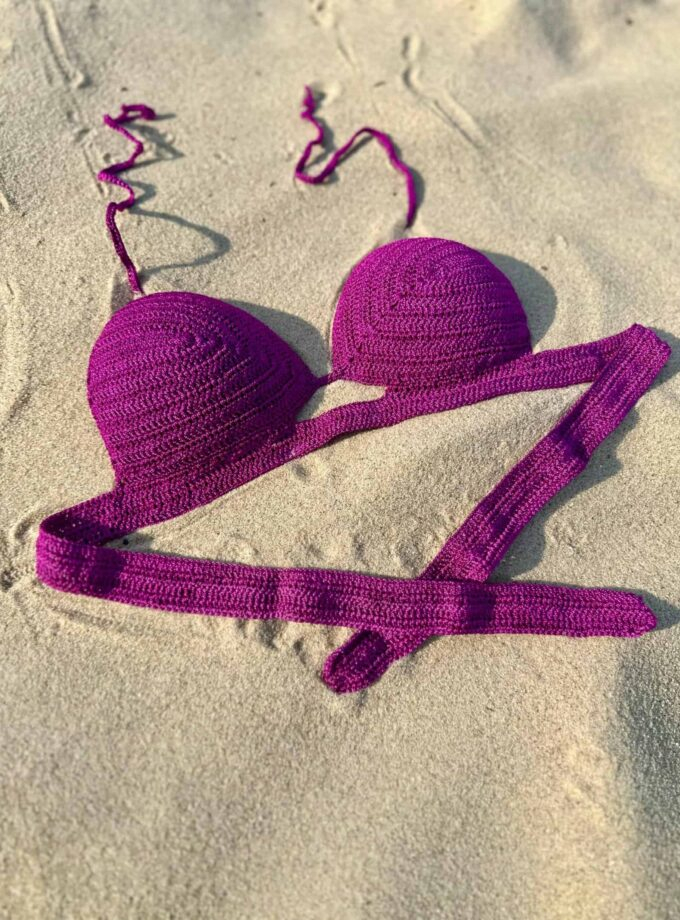 Vibrant purple crochet bikini top and bottom set laid on sandy beach with bright sunlight, showcasing stylish swimwear perfect for summer beach trips and ocean escapes.