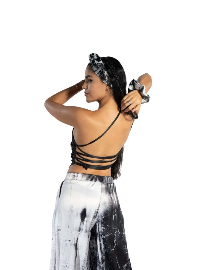 Elegant woman with long dark hair wearing trendy black and white tie-dye outfit, headband, and matching scrunchie, posing confidently against plain white background.