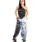 Stylish young woman wearing a black satin one-shoulder top and black-and-white tie-dye paint splatter baggy pants with platform heels for a trendy fashion look.