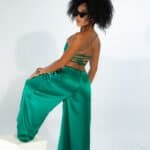 Luxury satin green pants and crop top fashion photo shoot, stylish woman with curly hair and sunglasses posing against white background, elegant summer clothing, contemporary fashion style, NYC fashion scene.