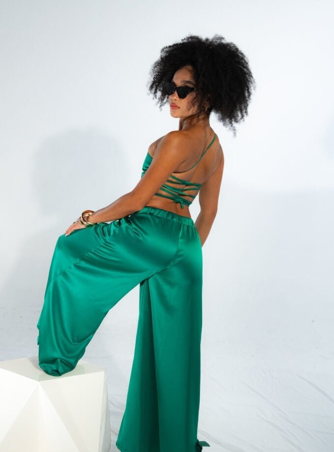 Luxury satin green pants and crop top fashion photo shoot, stylish woman with curly hair and sunglasses posing against white background, elegant summer clothing, contemporary fashion style, NYC fashion scene.
