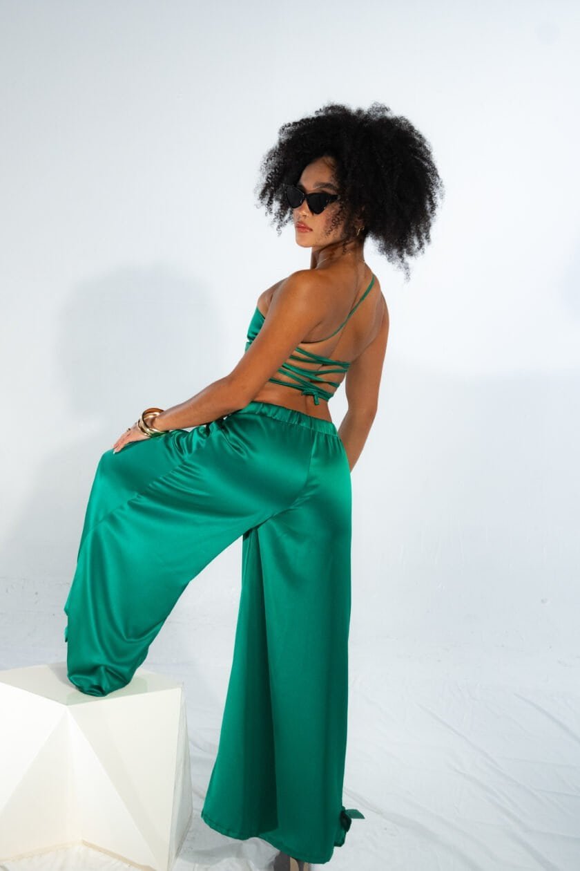Luxury satin green pants and crop top fashion photo shoot, stylish woman with curly hair and sunglasses posing against white background, elegant summer clothing, contemporary fashion style, NYC fashion scene.