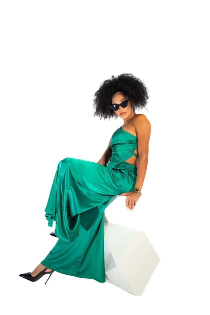 Luxury green satin evening gown, woman wearing stylish black sunglasses, elegant fashion with high heels and jewelry, modern glamour attire, black curly hairstyle, fashion photography.