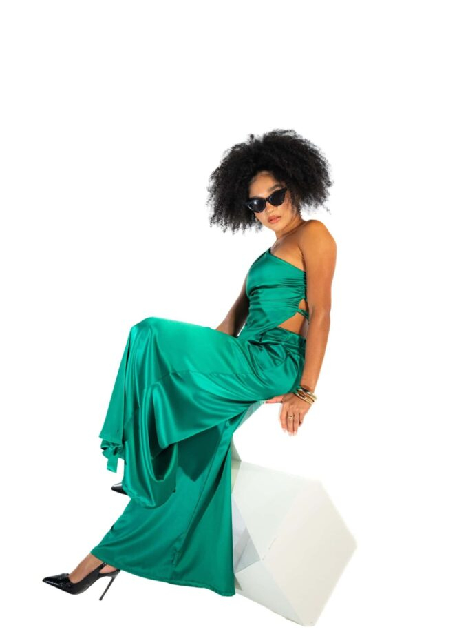 Luxury green satin evening gown, woman wearing stylish black sunglasses, elegant fashion with high heels and jewelry, modern glamour attire, black curly hairstyle, fashion photography.