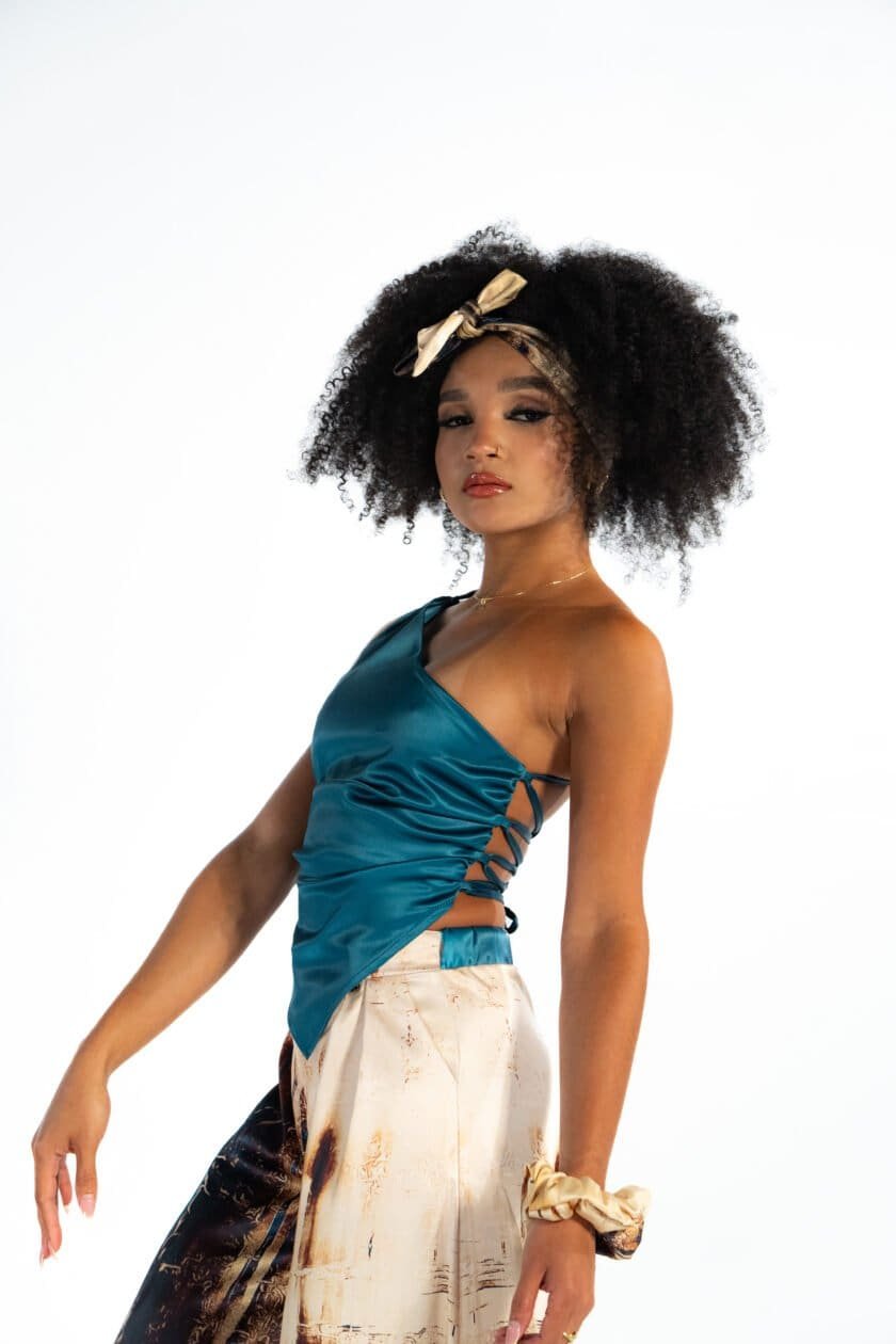 Luxury fashion model wearing stylish satin top and printed pants, accessorized with scrunchie and gold jewelry, fashion photography, trendy clothing, elegant style, contemporary runway look.