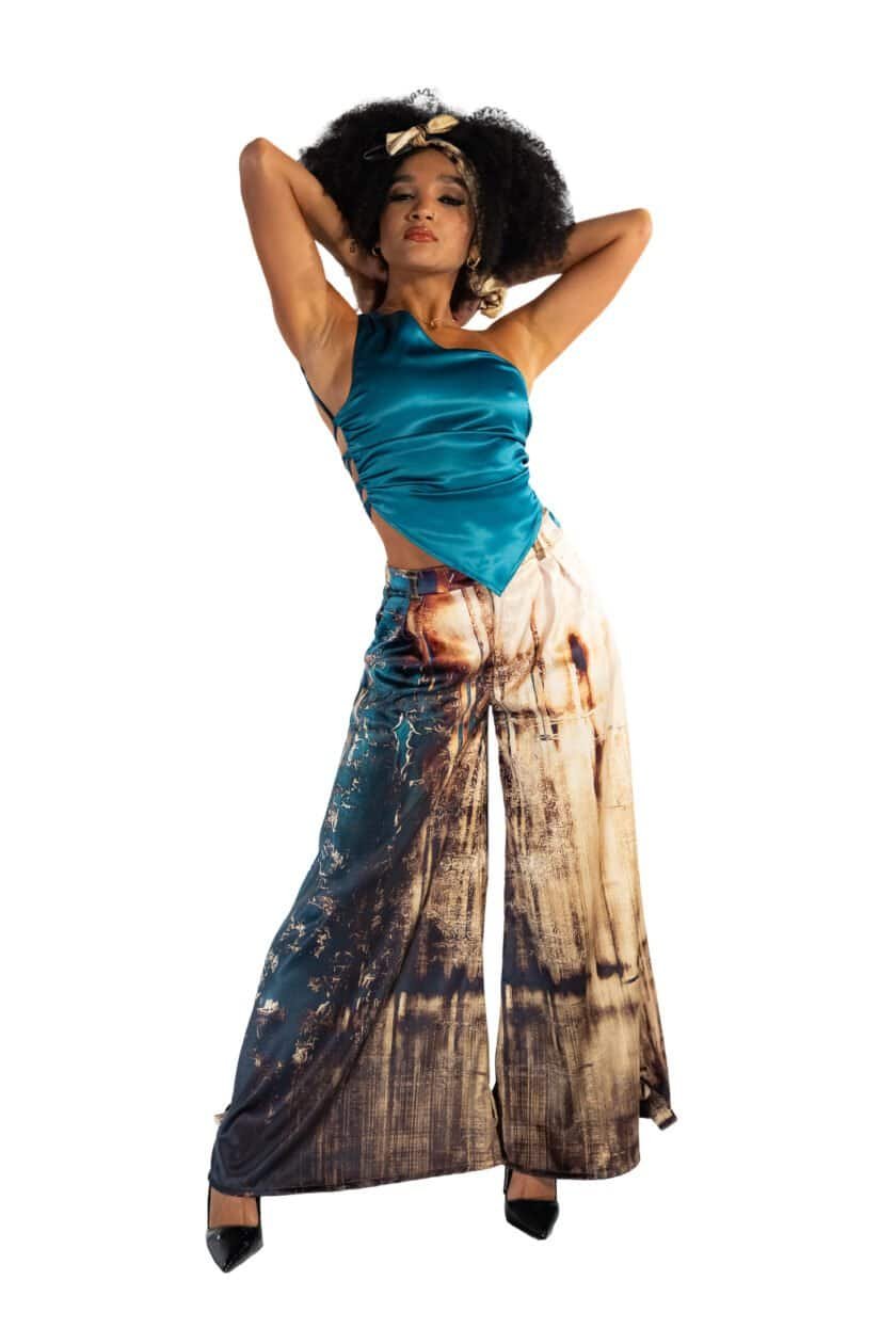 Rocker woman with natural Afro hairstyle and bold fashion pose, wearing a blue satin top and wide-leg printed pants, showcasing trendy street style and confident attitude.