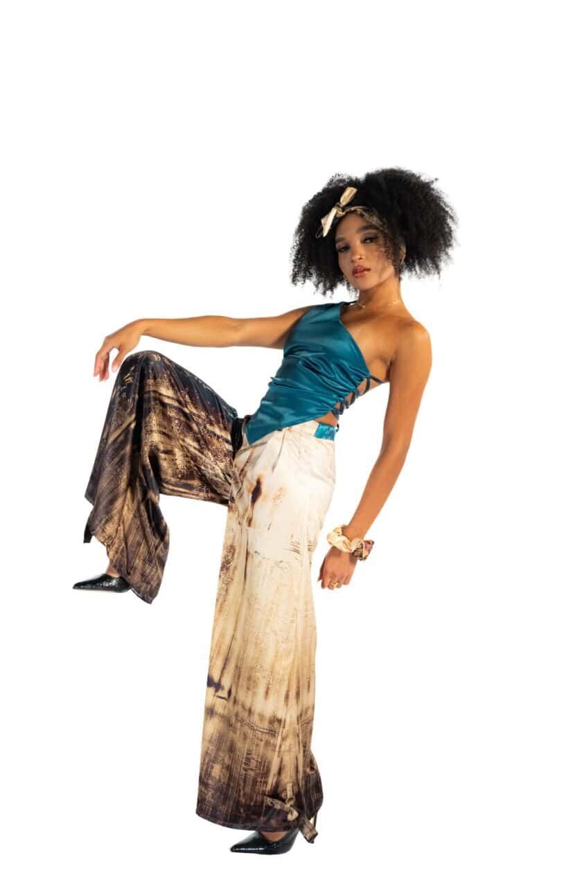 Elegant woman in stylish blue satin top and wide-leg printed pants posing against a white background, showcasing African-inspired fashion and accessories.