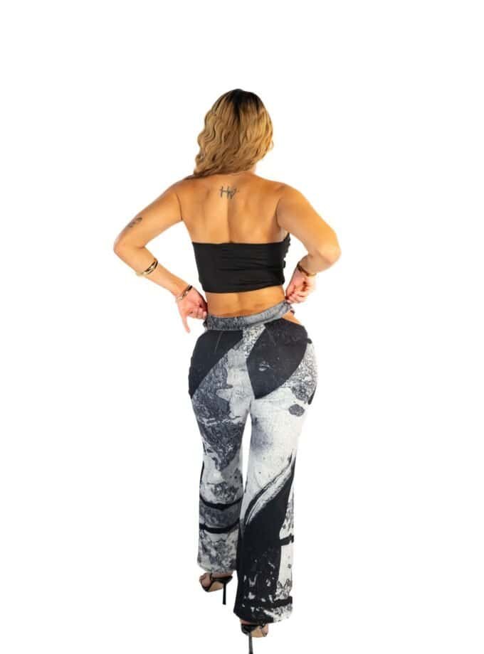 Richly textured woman in stylish black crop top and artistic patterned pants, standing confidently with hands on hips, isolated against white background, showcasing trendy fashion and jewelry for modern style.