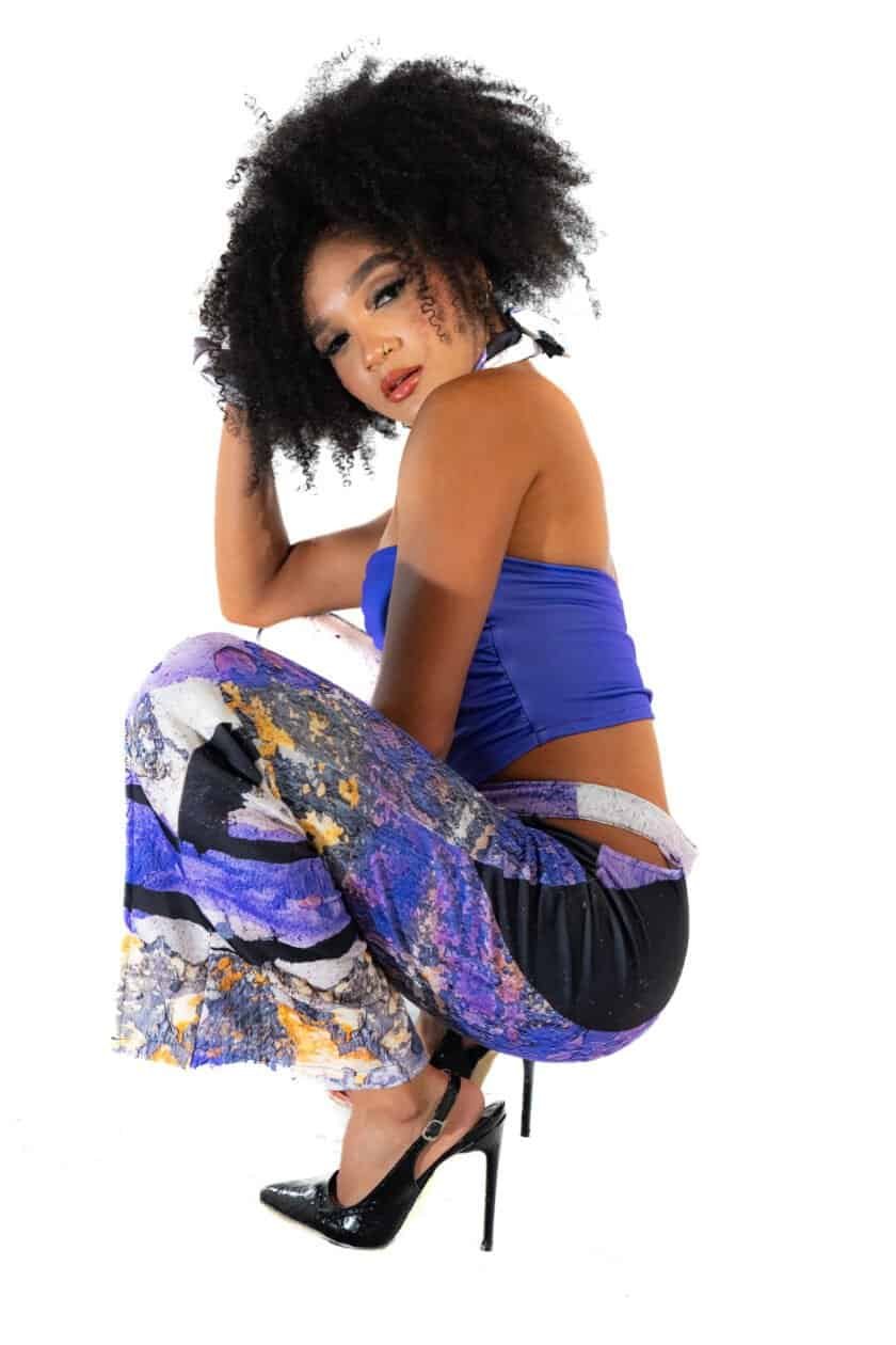 Richardson floral pants, black heels, blue crop top, curly hair, urban fashion, stylish woman, modern streetwear, model pose, vibrant outfit, fashion photography, lifestyle, trendy clothing, confident look, chic style, contemporary fashion.