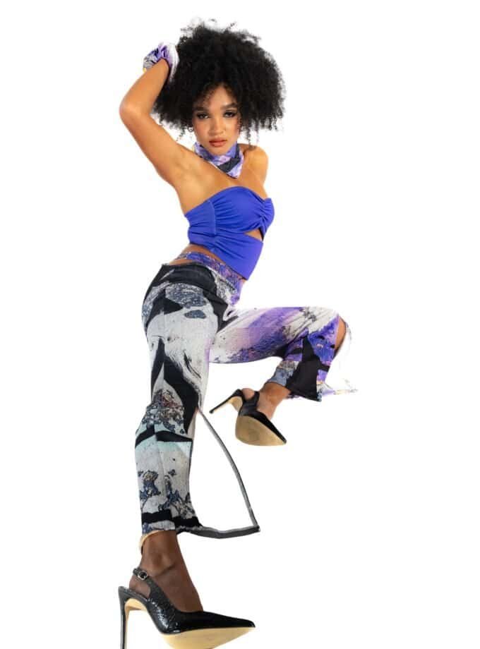 Bold woman in vibrant blue top, patterned wide-leg pants, high heels, and purple accessories, striking a confident pose for Confiture NYC fashion showcase.
