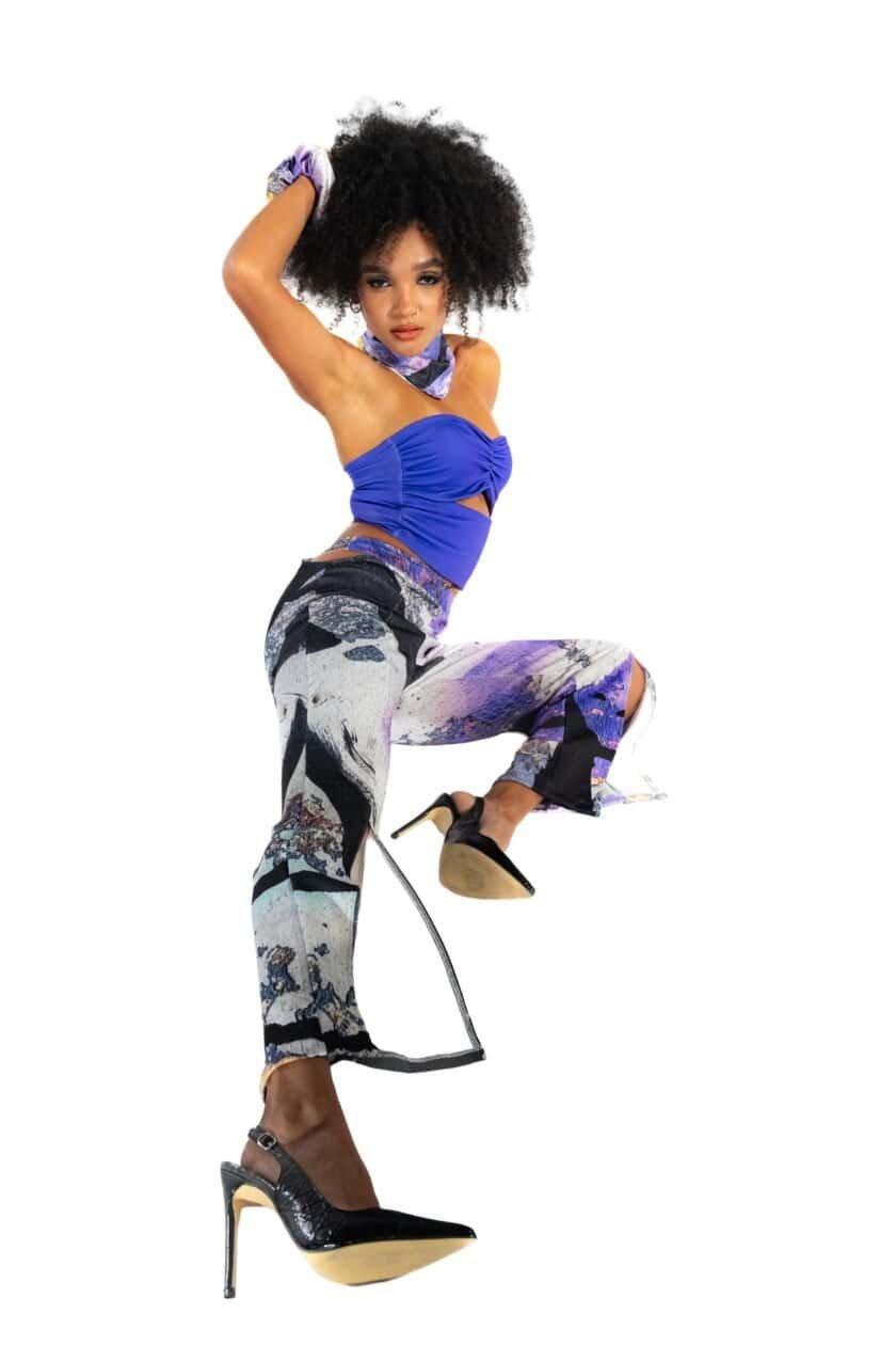Bold woman in vibrant blue top, patterned wide-leg pants, high heels, and purple accessories, striking a confident pose for Confiture NYC fashion showcase.