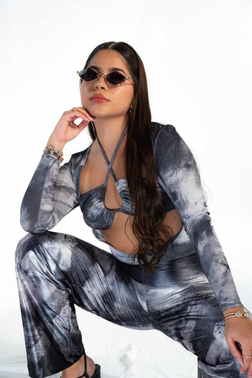 Vintage-inspired woman wearing sunglasses and a stylish tie-dye matching top and pants set, seated in a confident pose, featuring accessories like bracelets, highlighting fashion, trendy outfits, and accessory styling.