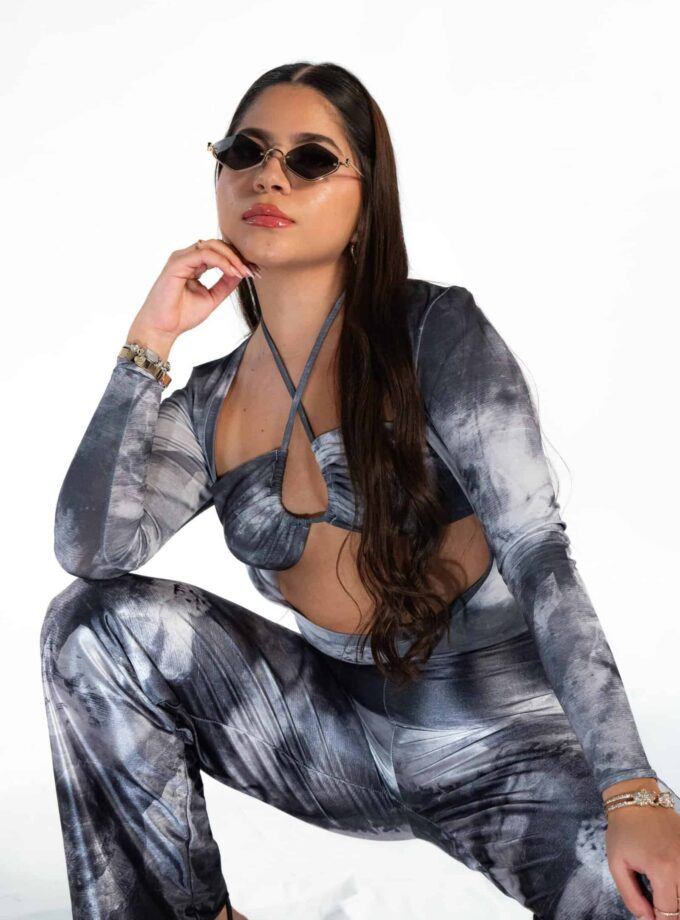 Vintage-inspired woman wearing sunglasses and a stylish tie-dye matching top and pants set, seated in a confident pose, featuring accessories like bracelets, highlighting fashion, trendy outfits, and accessory styling.