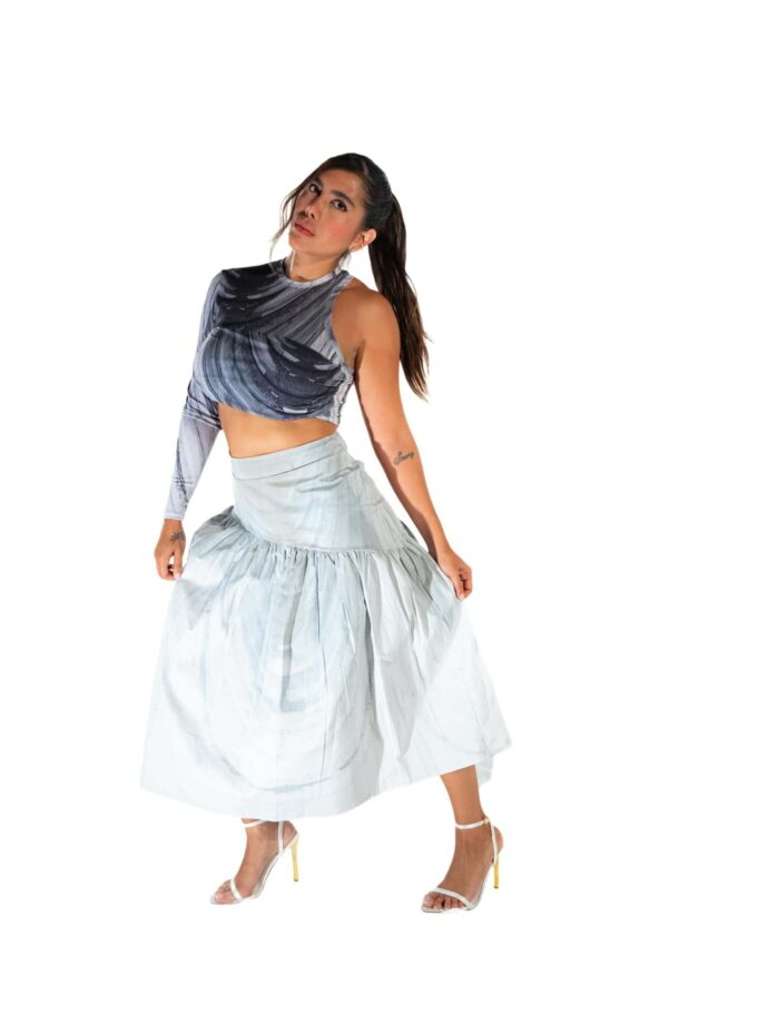 Vibrant woman wearing a black and white printed crop top with a long white skirt, standing confidently against a white background, showcasing unique fashion style.