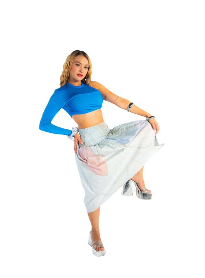 Vibrant woman in bold blue crop top, flowing floral skirt, and silver platform heels posing confidently for fashion shoot.