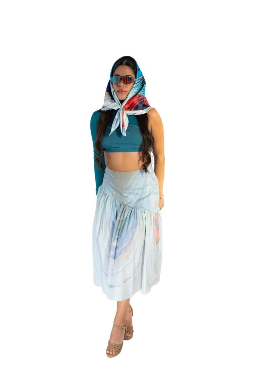 Bold woman in stylish blue crop top, flowing pastel skirt, colorful scarf, and trendy sunglasses, embodying summer fashion and chic accessories.