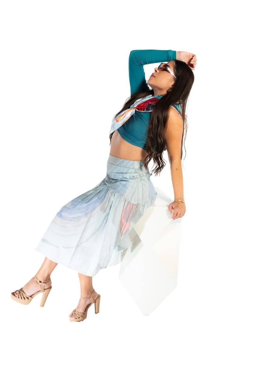 Vibrant fashion-forward woman wearing a colorful crop top, flowing skirt, and high heels against a white background, showcasing stylish summer or casual look.