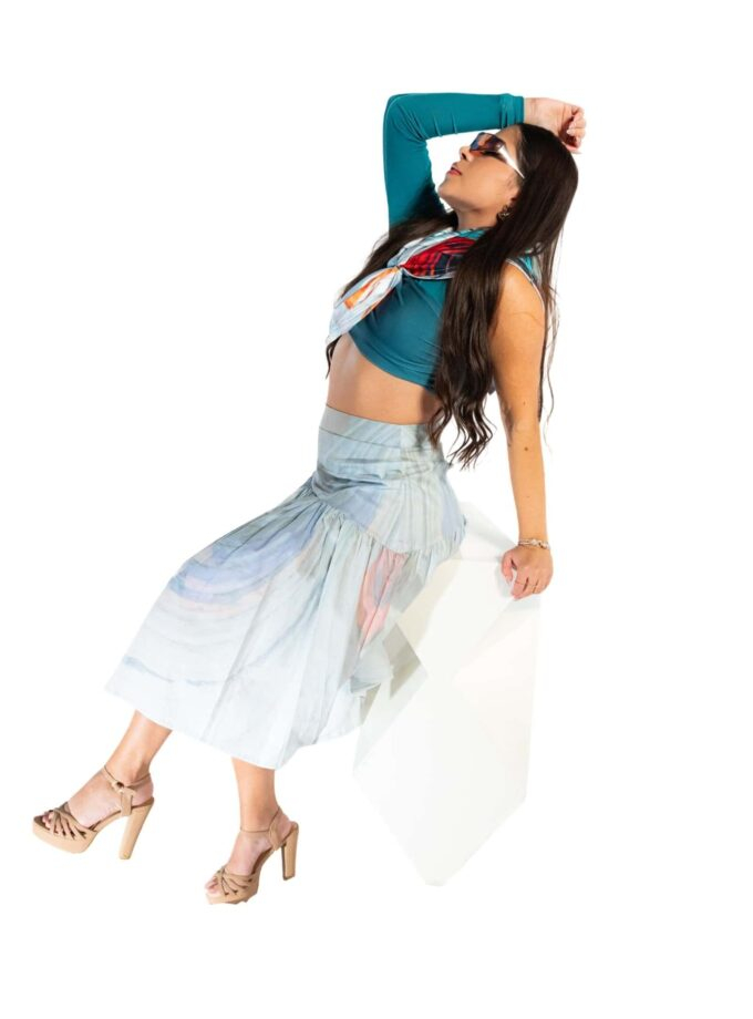Vibrant fashion-forward woman wearing a colorful crop top, flowing skirt, and high heels against a white background, showcasing stylish summer or casual look.