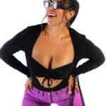 "Woman laughing wearing 3D glasses, black crop top, and purple pants, showcasing playful fashion and vibrant style, with a black purse and jewelry, on a white background.".